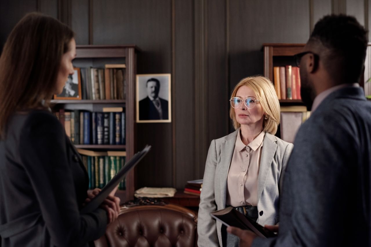 gallery-5 Three business professionals engage in a serious meeting in an executive office setting.
